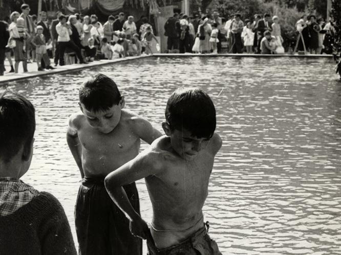 Niños bañándose en una pileta pública frente a feria de artes plásticas
