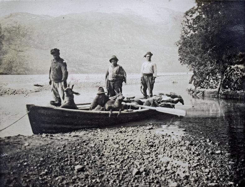 Cuatro trabajadores en un bote sobre un remanso del río Baker, posando con huemules cazados